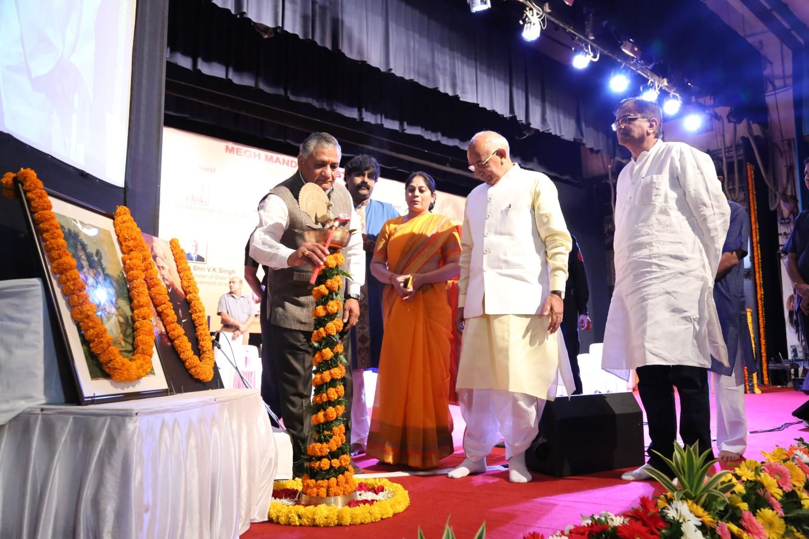 A guest of honour lighting the ceremonial lamp beside a garlanded painting